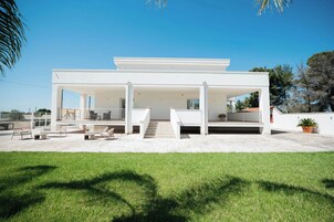 A modern white building with a covered outdoor area, a staircase leading to a second level, and a grassy foreground.