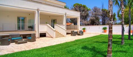 A modern house with a covered patio, outdoor seating, and a well-maintained lawn.
