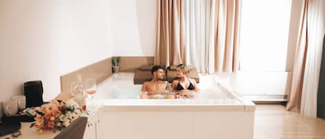 A room with a bathtub, a table with a bouquet of flowers, and a coffee maker.