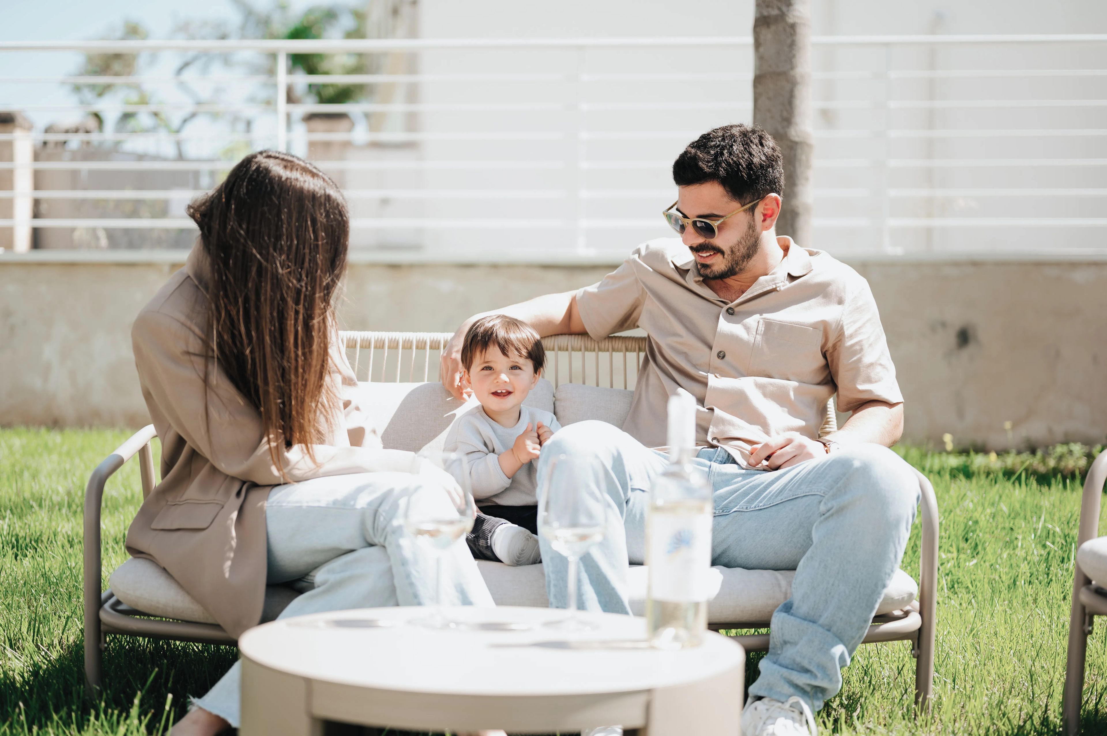 A family of three seated on a bench outdoors with a table in front of them.