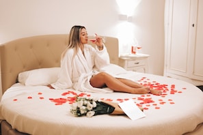 A person sitting on a bed with rose petals scattered on it, holding a glass. - Dimore Relais - Suite Garden Breakfast (Porto Cesareo)