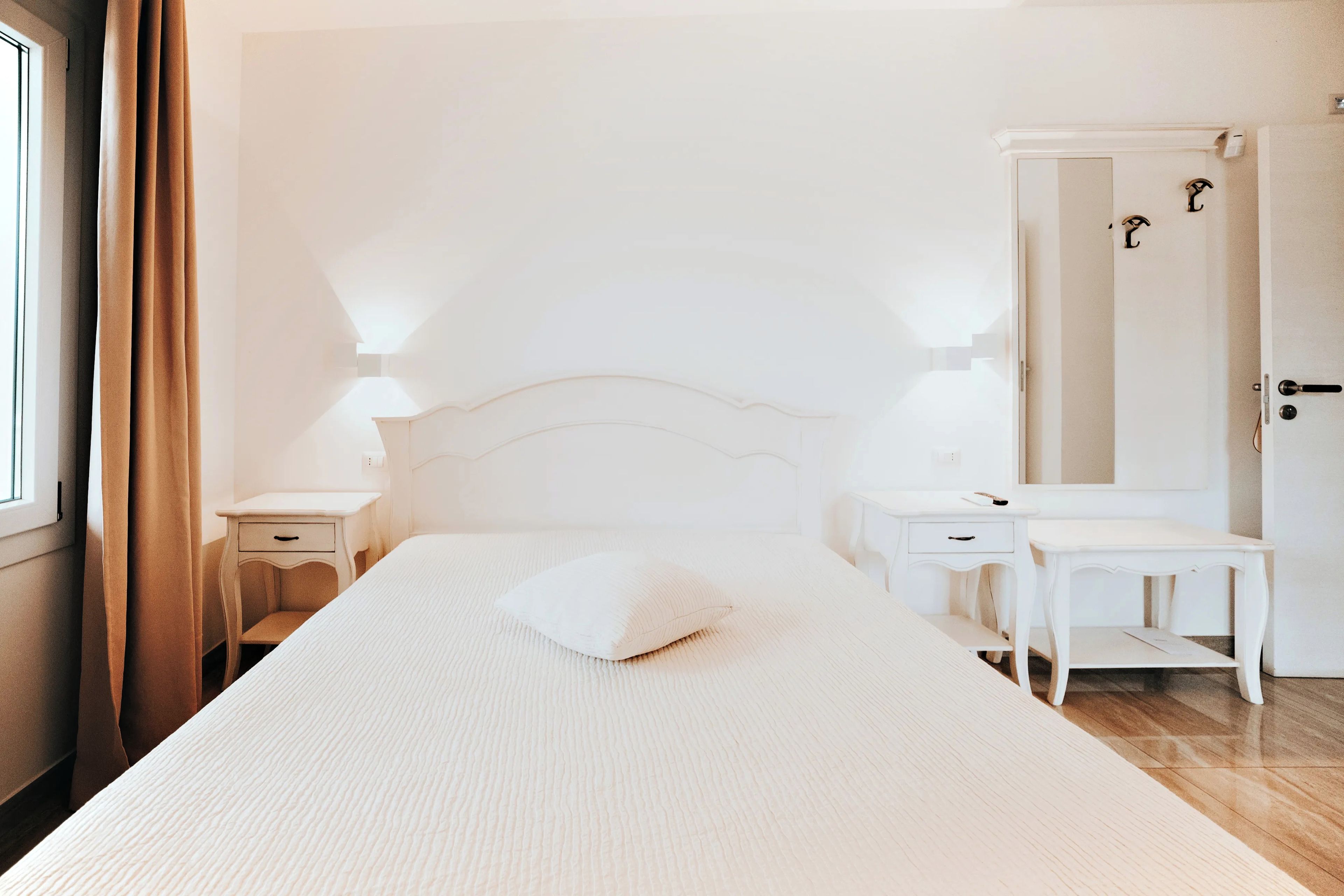 A bedroom with a bed, bedside tables, a nightstand, a dresser, a mirror, and a door.