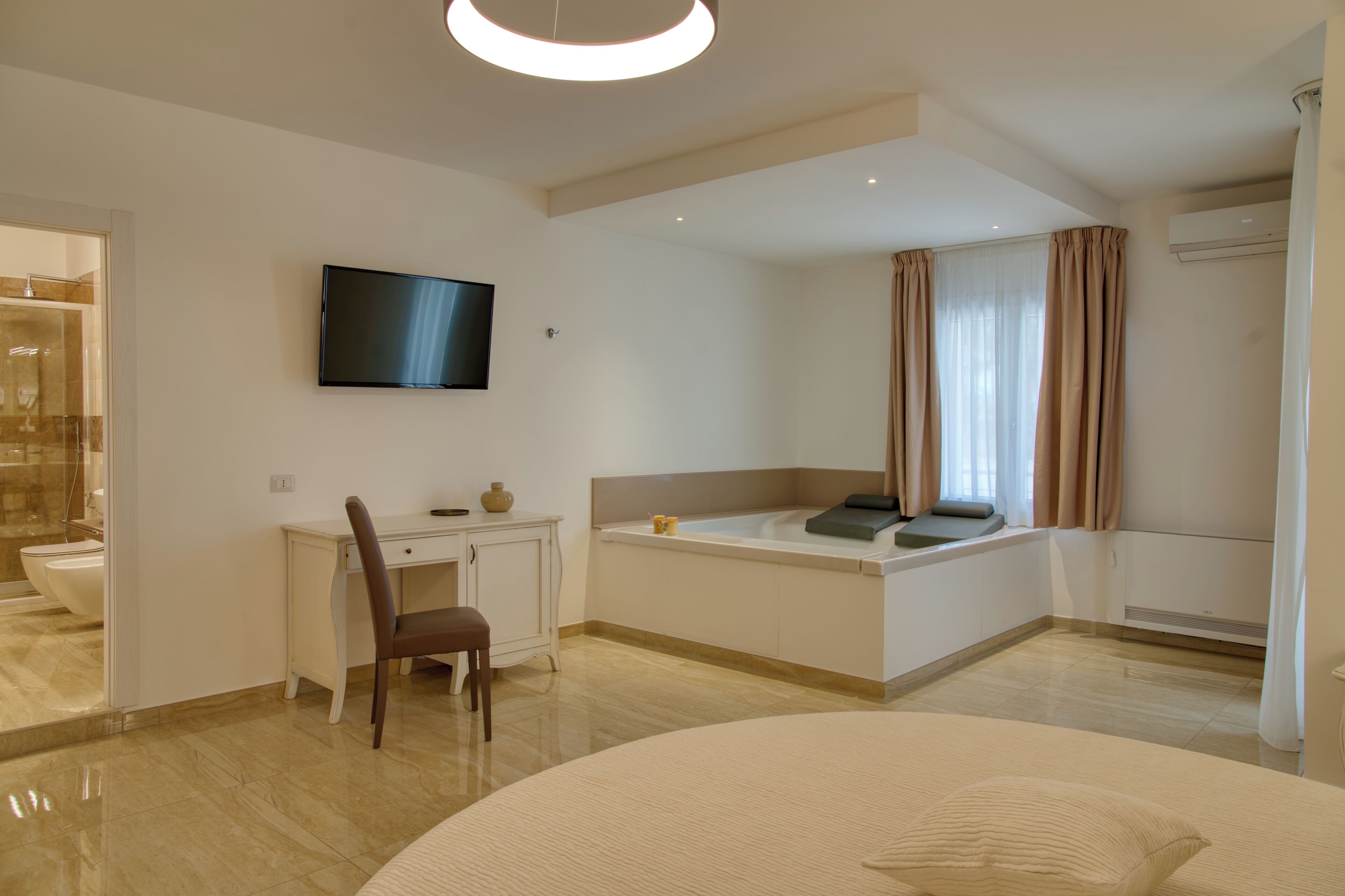 A modern hotel room with a bed, a desk, a TV, a bathtub, and a shower area.