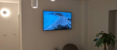 Una habitación moderna con televisor de pantalla plana en la pared, un sillón cómodo, una mesita auxiliar con una planta e iluminación empotrada en el techo.