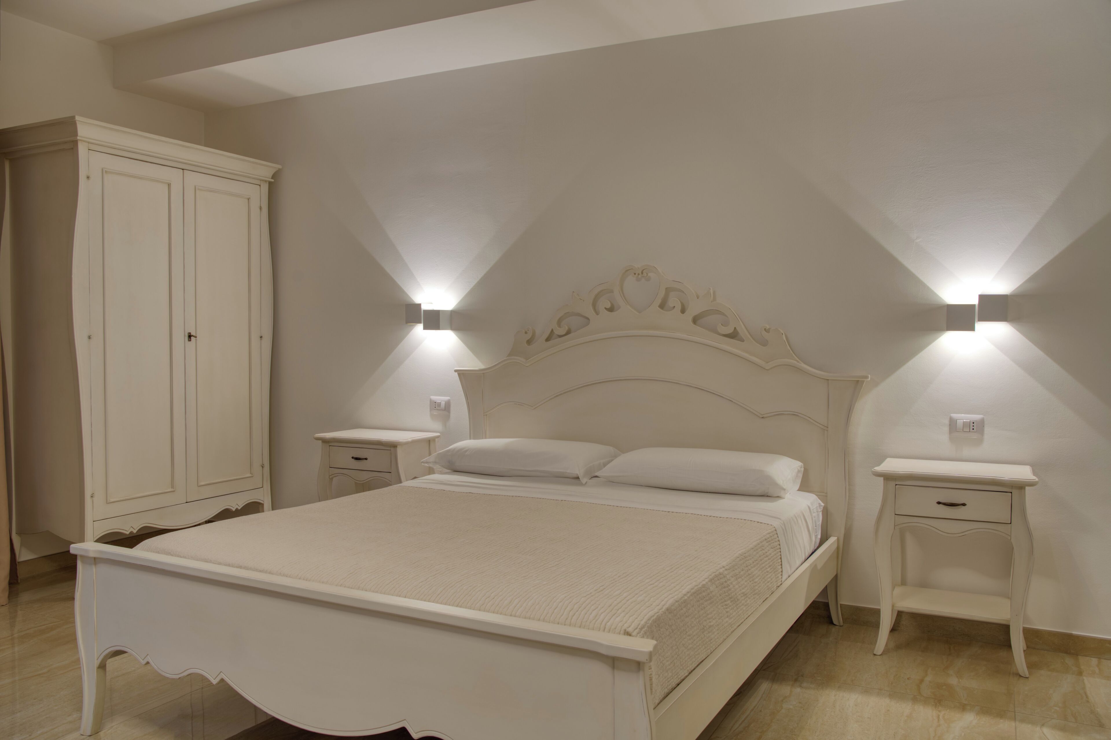 A bedroom with a bed, nightstands, a wardrobe, and wall-mounted lights.