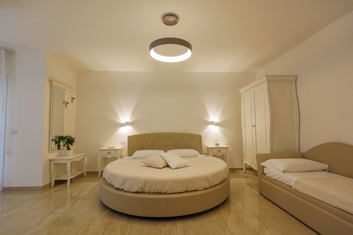 A circular bed with a headboard, bedside tables, and wall-mounted lights.