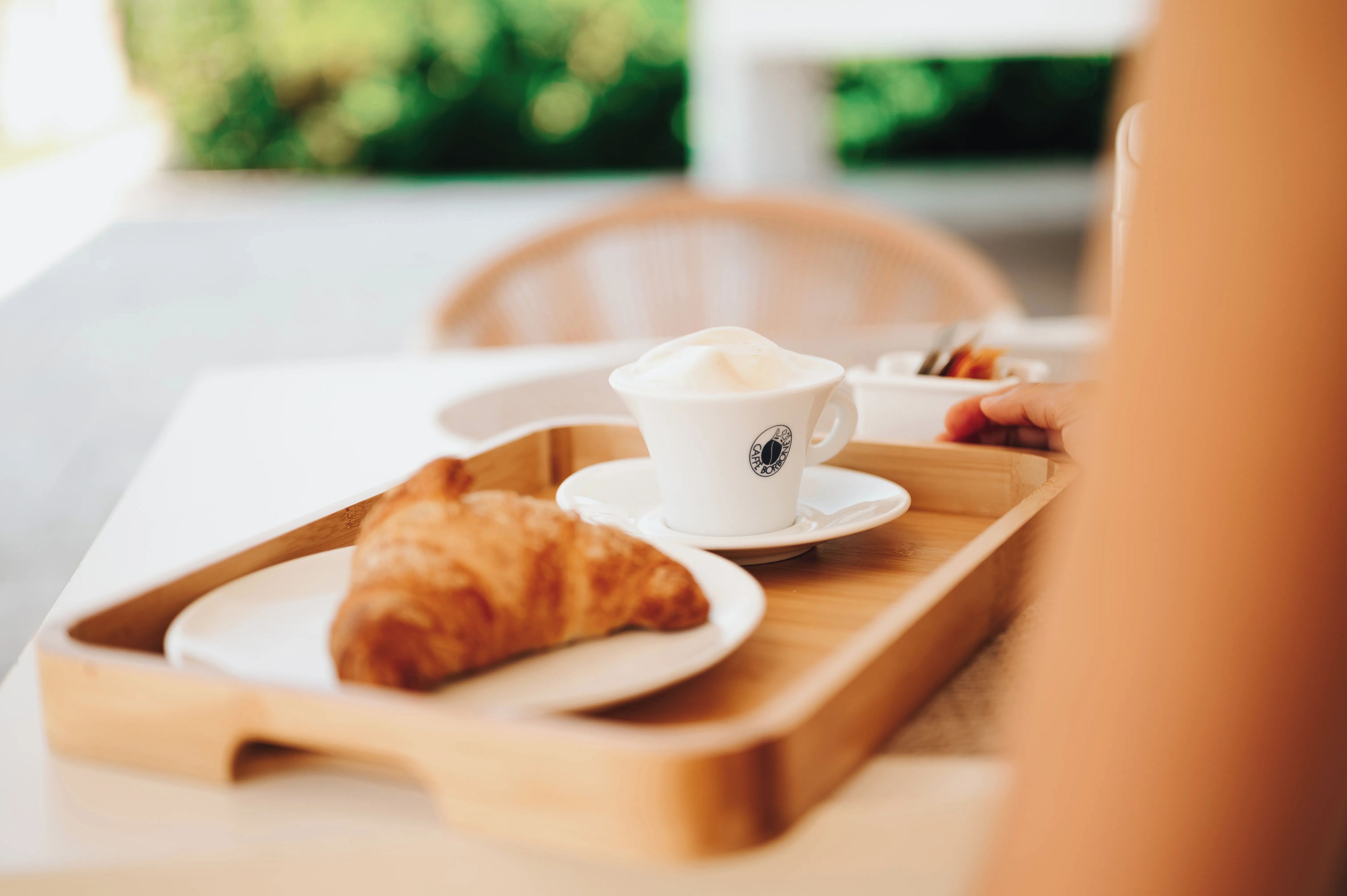 A tray with a cup of coffee and a croissant on a table.