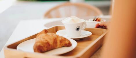 A tray with a cup of coffee and a croissant on a table.