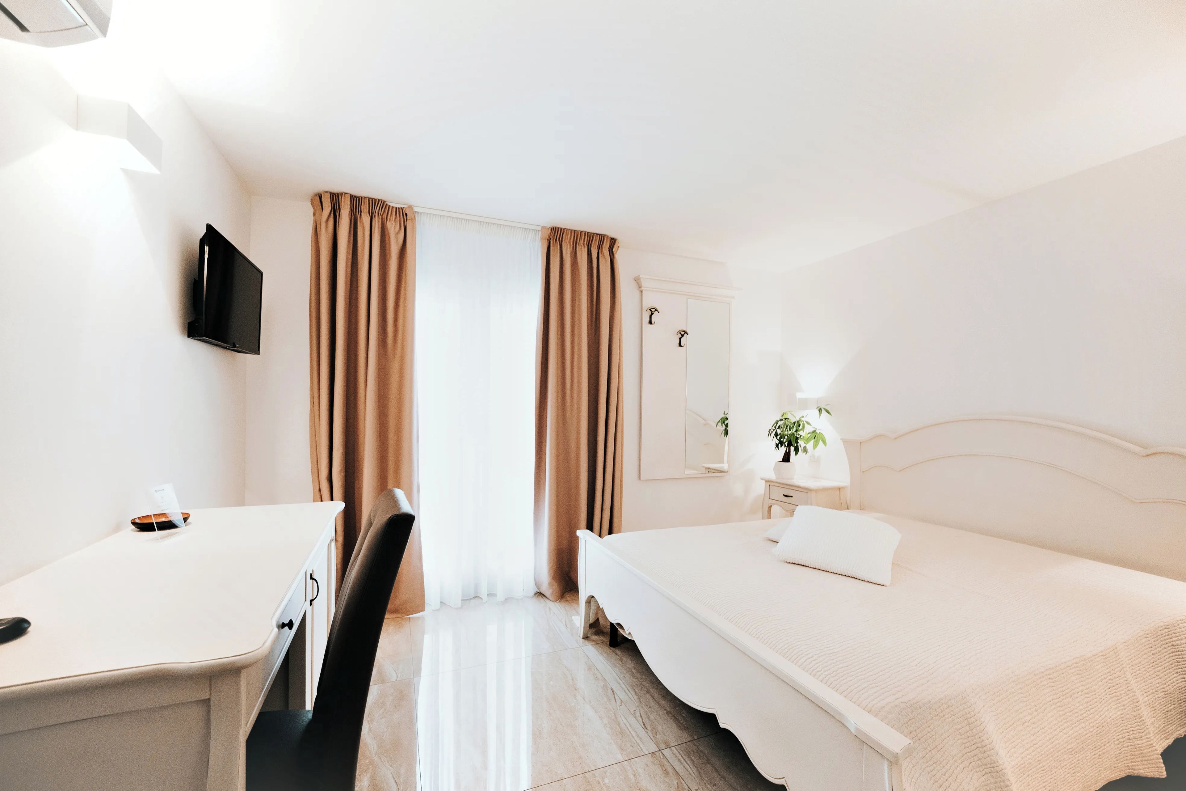 A hotel room with a bed, a desk, a chair, a TV, and a window with curtains.