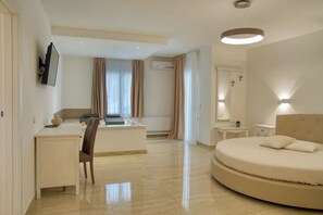 A modern hotel room with a round bed, a desk with a chair, a small table, and a TV mounted on the wall. - Dimore Relais - Suite Garden Breakfast (Porto Cesareo)
