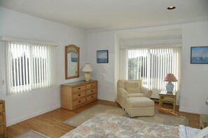 Un dormitorio con una cama, un aparador, una silla y dos ventanas con persianas.