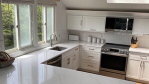 A modern kitchen with white cabinetry, a large island with a marble countertop, an LG oven, and a window overlooking greenery. - Gorgeous South Beach Contemporary 5 min walk to beach with AC, and WiFi (Edgartown)