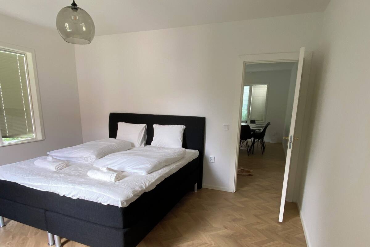 Une chambre avec un grand lit, un luminaire au plafond et un plancher en bois.