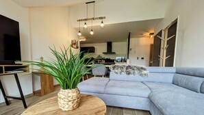 Una sala moderna con un sofá seccional gris, una mesa de centro de madera con una planta tejida, y una alfombra mullida.