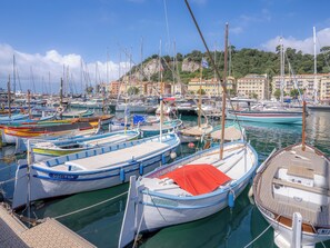A marina with various boats docked, a clear sky, and buildings in the background.