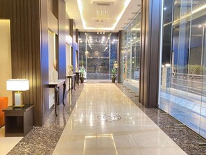 A modern hotel lobby with a polished marble floor, a reception desk, and a glass wall offering a view of the street. - فندق فصل الصيف امان المنسك (Abha)