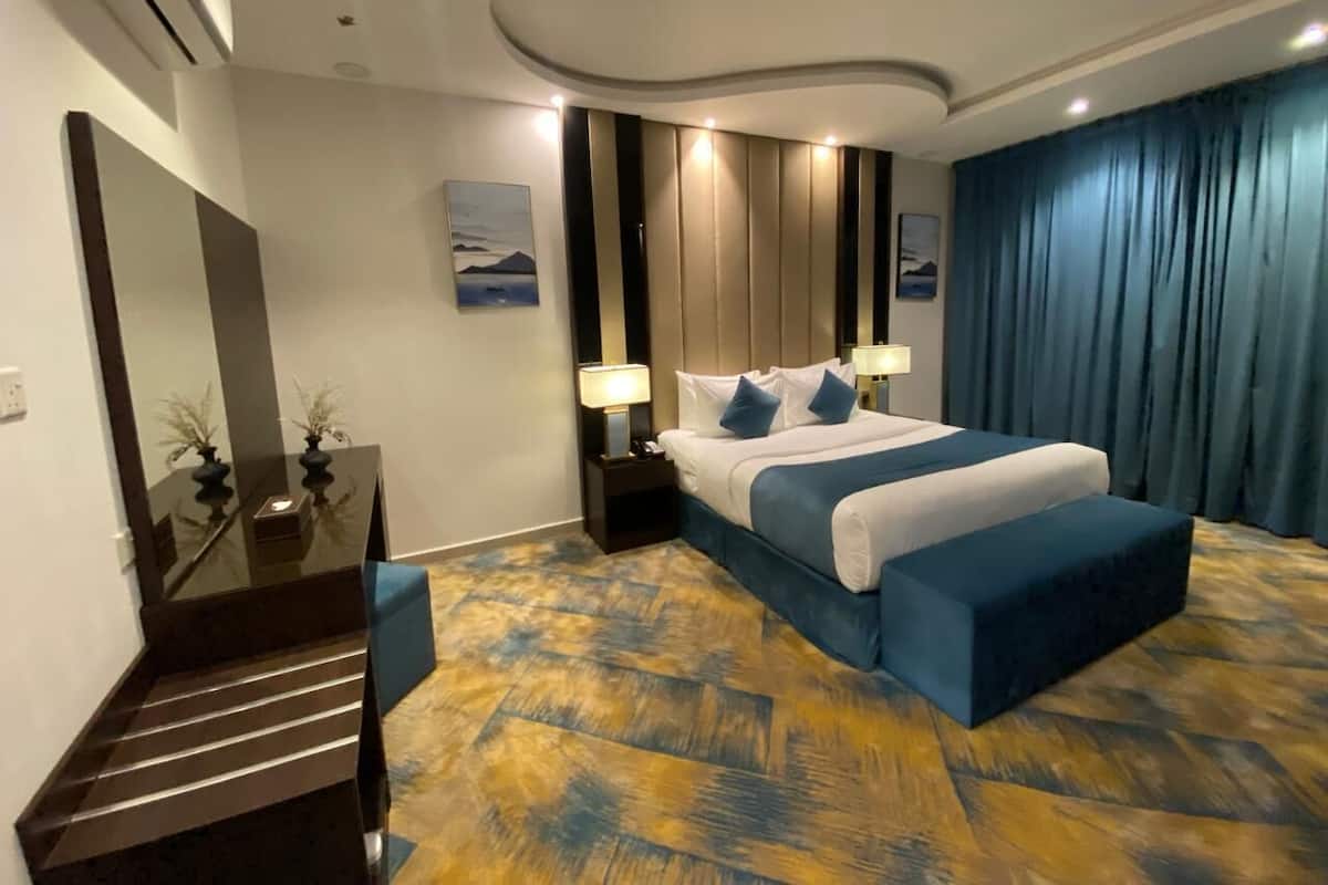 Quarto de hotel com cama, mesas de cabeceira, escrivaninha, espelho e escada.