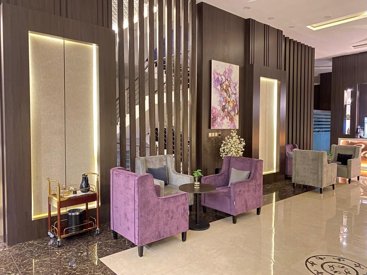 A modern lobby with a seating area featuring purple armchairs, a small round table, and a decorative cart.