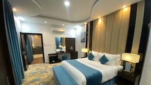 Habitación de hotel con una cama grande, un escritorio, una silla y un baño visible a través de una puerta abierta.