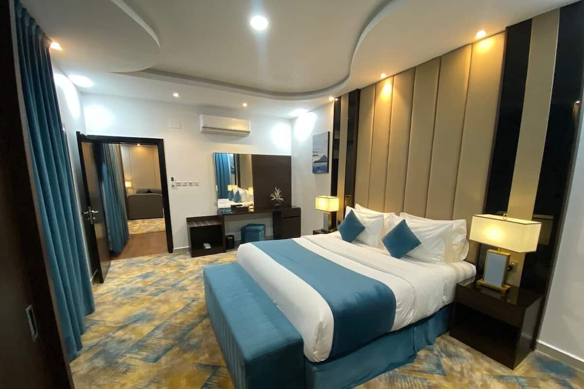 Quarto de hotel com uma cama grande, uma escrivaninha, uma cadeira e um banheiro visível por uma porta aberta.