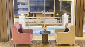 Un vestíbulo con dos sillones, una mesita redonda con un florero, y un ventanal que ofrece vistas a un edificio y unas escaleras.