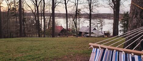 A hammock in a grassy area with trees and a lake view.