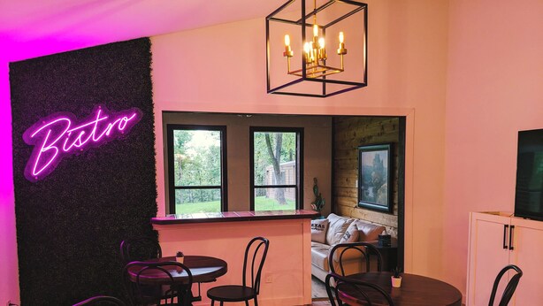 Una habitación acogedora con un letrero de neón que dice "Bistro", muebles de madera, una araña y vistas al exterior.