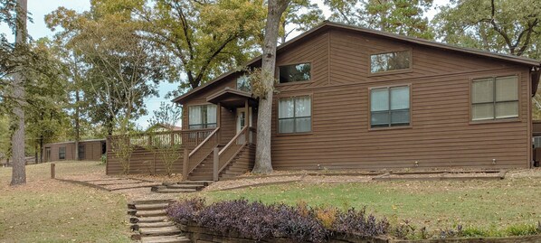 A two-story wooden cabin with a staircase leading to the entrance, surrounded by trees and a grassy area. - Sprawling 3-bedroom house in delightful Scroggins with WiFi, AC and lakeview (Scroggins)