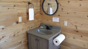 Un bagno in una cabina di legno con lavandino, specchio, porta asciugamani e cartello di avvertimento.