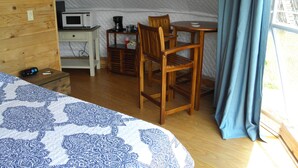 Una sistemazione in tenda con un letto, una scrivania con un forno a microonde, una sedia e un tavolo.