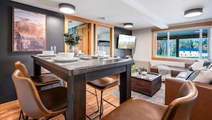 A modern living room with a dining area, featuring a dark wooden table, leather chairs, and a large window offering a view of the outdoors. - Buck's Den - Snowmobile Trails, Trailer Parking, Near hiking, golfing, Sugarloaf (Eustis)