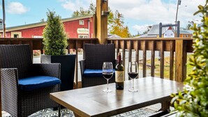 An outdoor seating area with wicker chairs and a table, a bottle of wine, and two glasses on the table. - Buck's Den - Snowmobile Trails, Trailer Parking, Near hiking, golfing, Sugarloaf (Eustis)