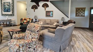 A living room with a large bear rug, two sofas, a patterned armchair, and a dining area with a checkered tablecloth. - New 4-bedroom for rent during EAA!  Sleeps 17, large loft and three bedrooms!  (Wautoma)