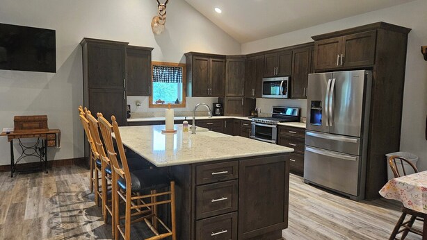 A modern kitchen with dark wood cabinets, a large island with bar stools, stainless steel appliances, and a mounted deer head on the wall. - New 4-bedroom for rent during EAA!  Sleeps 17, large loft and three bedrooms!  (Wautoma)