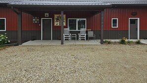 A red building with a covered porch, two white chairs, and a small table. - New 4-bedroom for rent during EAA!  Sleeps 17, large loft and three bedrooms!  (Wautoma)