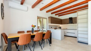Un comedor moderno con una mesa y sillas de madera, un jarrón con flores, y una cocina con armarios blancos y una campana extractora negra.