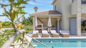 Un área junto a la piscina con sillones de descanso y sombrillas, un techo de azulejos y un pilar de piedra.