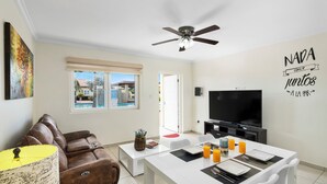 A modern living room with a brown leather sofa, a white dining table set with orange juice, and a flat-screen TV.