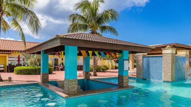 A pool area with a covered pavilion, palm trees, and a clear blue sky.