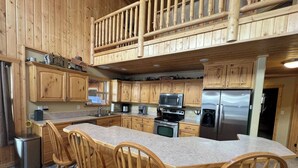 Una cocina tipo cabaña de madera con una isla central, sillas de madera y un microondas empotrado.