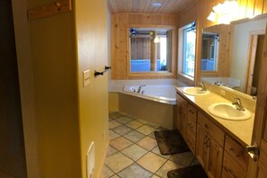 Une salle de bain avec des murs en bois, une baignoire, deux lavabos et un grand miroir.