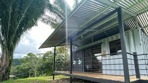 A modern building with a metal roof and wooden deck, surrounded by lush greenery and palm trees.