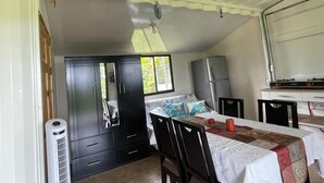 A compact room with a bed, a small table, a chair, a wardrobe, and a kitchenette.