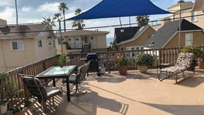 Un patio con una mesa, sillas, una parrilla y plantas en macetas.