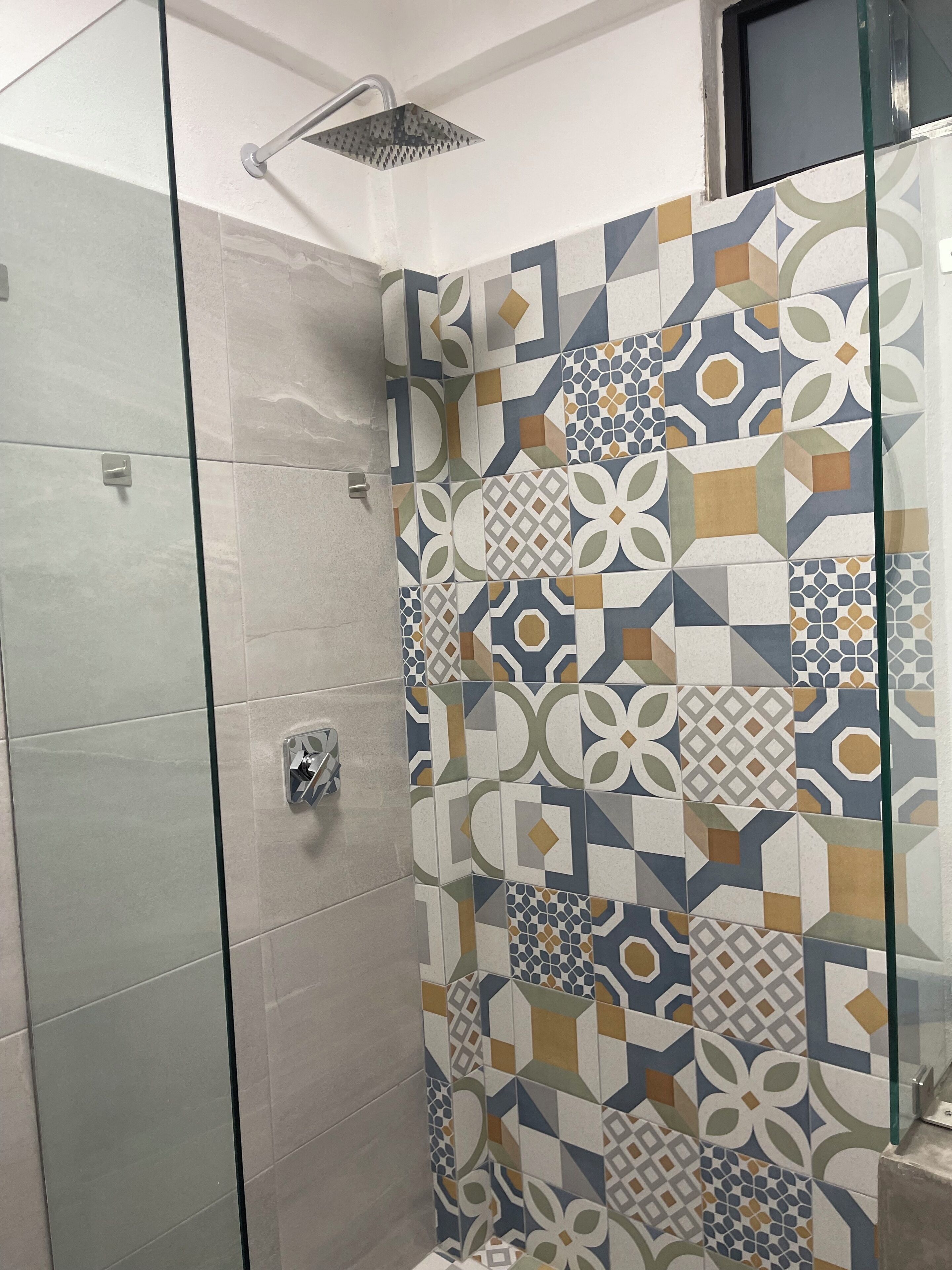 A shower area with a glass door and a tiled wall featuring geometric patterns.