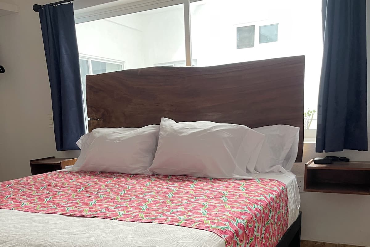 A neatly made bed with a patterned bedspread, a wooden headboard, and a nightstand with a remote control.