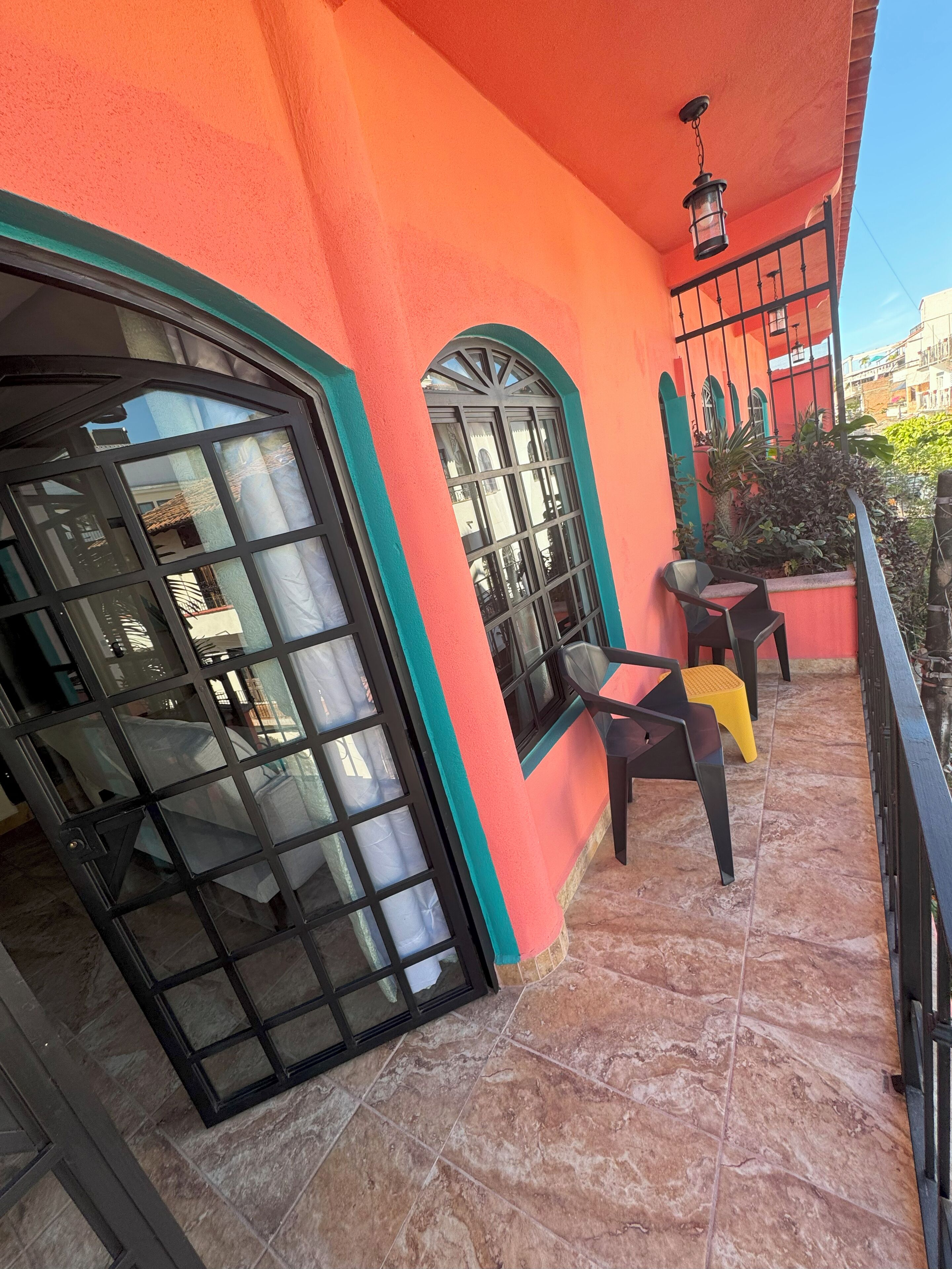 A balcony with a tiled floor, a black metal gate, and two chairs.