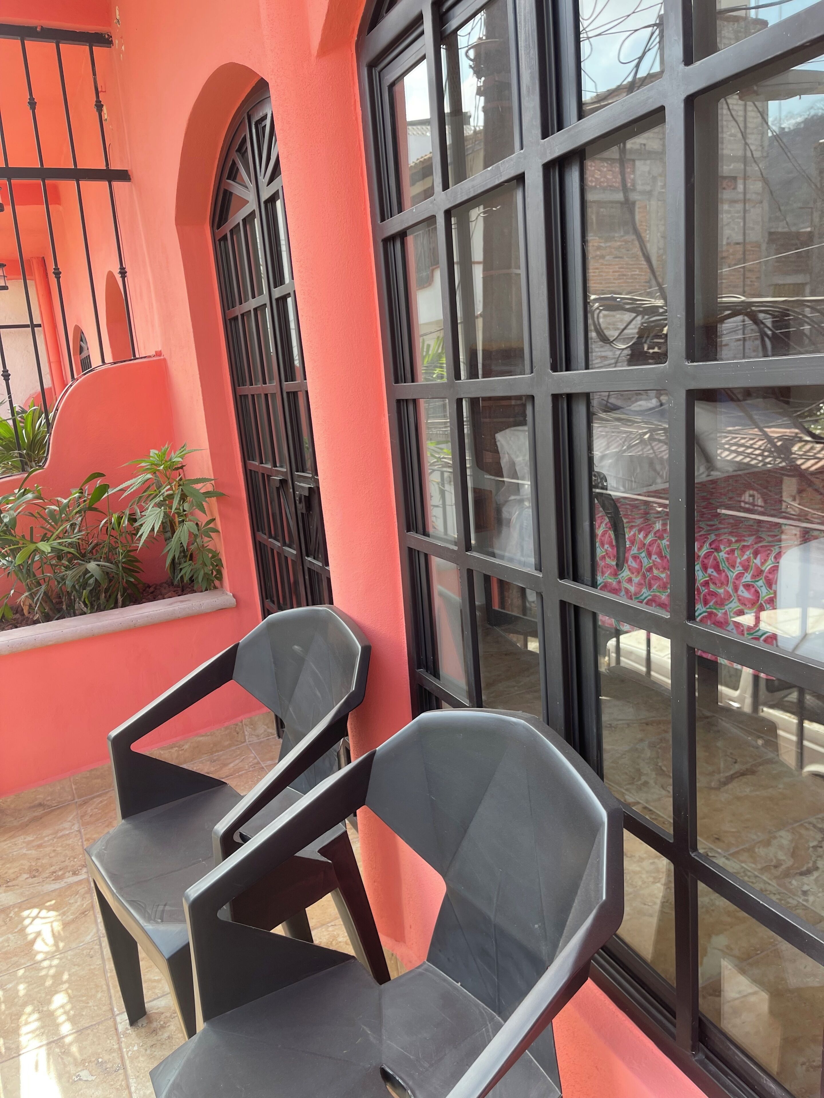 A room with a large window, a red wall, and two black chairs.