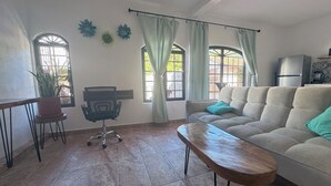 Een woonkamer met een bank, een houten salontafel, een bureau met stoel, en een potplant.
