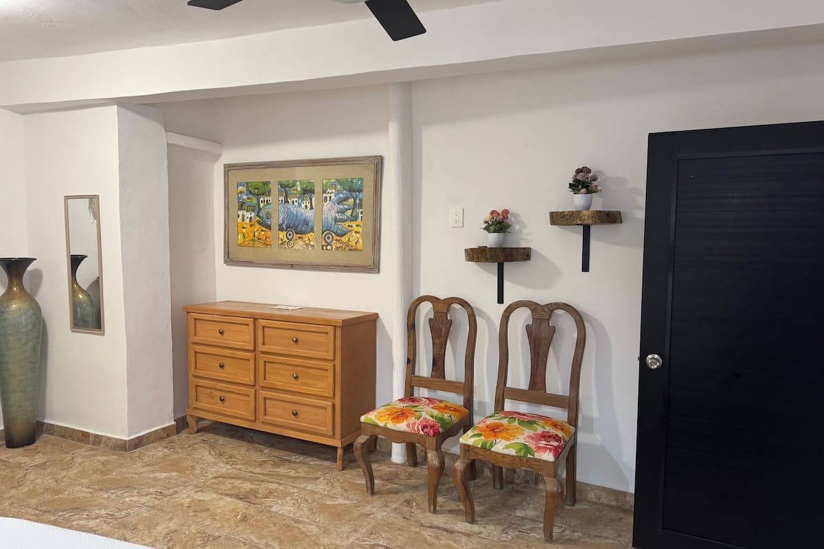 A hallway with a wooden dresser, two chairs with floral upholstery, a painting on the wall, and a black door.
